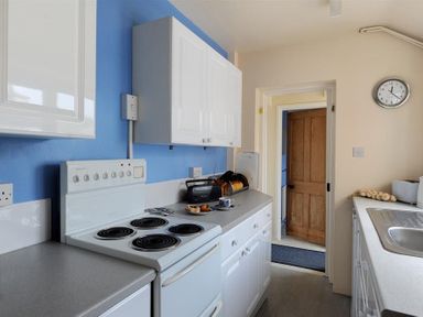 A kitchen with white cabinets an electric stove a toaster a cup with a plate and a wooden door at 23 Lym Close Lyme Regis