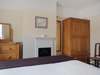 A bedroom with a bed a wooden wardrobe a wooden dresser with a mirror a chair and a fireplace at 23 Lym Close in Lyme Regis
