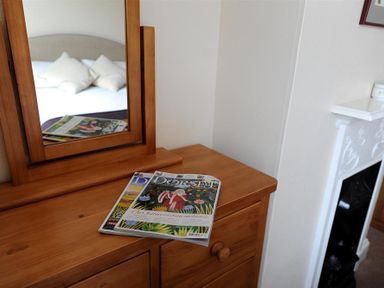 A wooden dresser with a mirror and magazines on top beside a white fireplace in a bedroom at 23 Lym Close Lyme Regis
