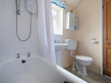 A bathroom with a bathtub shower sink toilet wall cabinet and wooden door at 23 Lym Close Lyme Regis