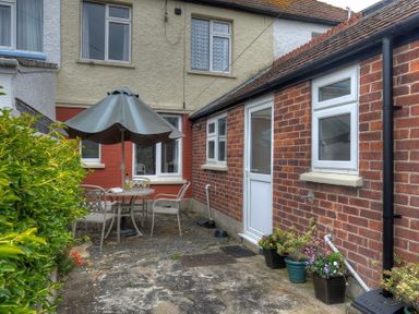 A small outdoor patio area with a round table, four chairs, an umbrella, and several potted plants at 23 Lym Close Lyme Regis
