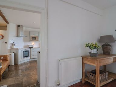 A kitchen with white cabinets a stove and a microwave seen through a doorway next to a wooden table with a lamp and flowers at Ancient Lights in Lyme Regis