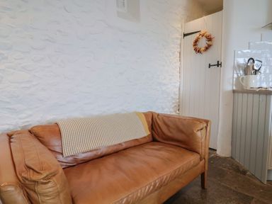 A brown leather sofa with a striped blanket on a white textured wall near a white door with a wreath and kitchen utensils in a container at Ancient Lights in Lyme Regis