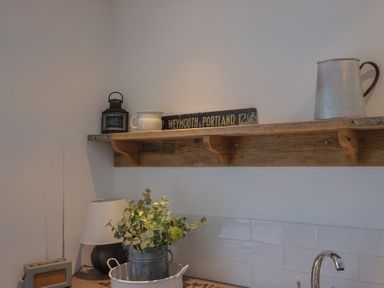 A wooden shelf with a lantern a white jug a metal pitcher and a sign above a kitchen countertop with a lamp a radio and a metal container with flowers at Ancient Lights in Lyme Regis
