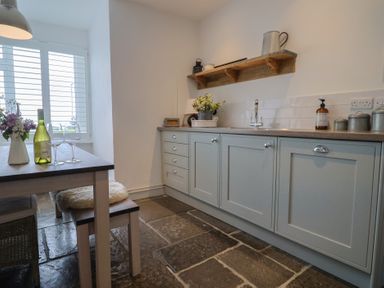 A kitchen with blue cabinets wooden countertop a dining table with wine glasses a bottle and flowers at Ancient Lights in Lyme Regis