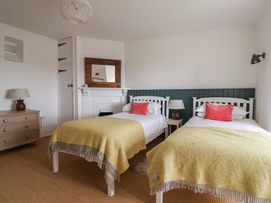 A bedroom with two single beds yellow blankets red pillows a wooden dresser and a mirror above a white fireplace at Ancient Lights in Lyme Regis
