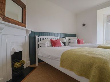 A bedroom with two single beds with white frames yellow blankets and red pillows next to a fireplace with flowers at Ancient Lights in Lyme Regis