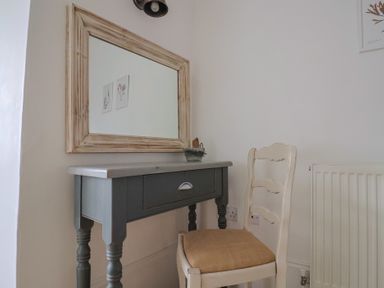 A gray wooden desk with a drawer under a large wooden framed mirror next to a white wooden chair with a woven seat at Ancient Lights in Lyme Regis
