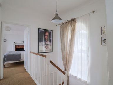 A hallway with a stair railing poster on the wall curtain on a window and a glimpse of a bedroom with a bed at Ancient Lights in Lyme Regis