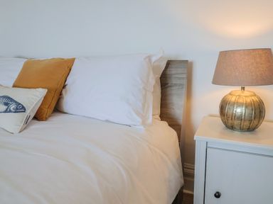 A bed with white and mustard pillows and a nightstand with a lamp at Ancient Lights in Lyme Regis