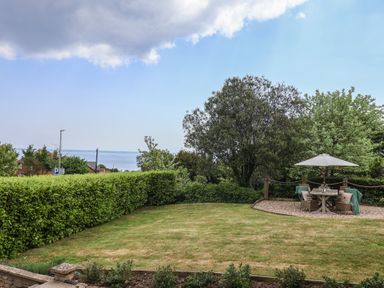 A garden with a trimmed lawn a seating area under an umbrella and trees at Ancient Lights in Lyme Regis