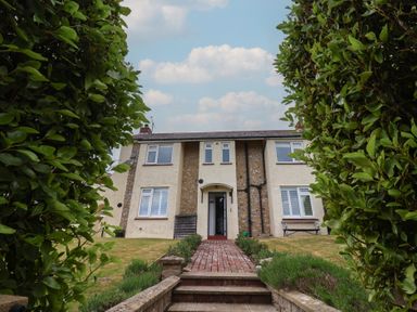 A two story house with a brick pathway and steps leading to the entrance framed by green bushes at Ancient Lights in Lyme Regis