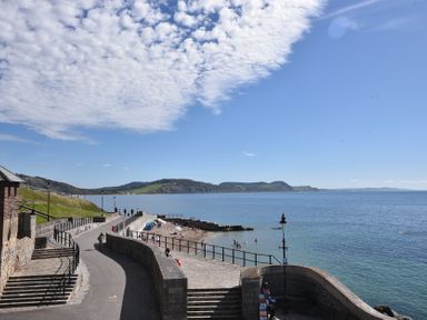 A coastal walkway with steps and a stone wall next to a beach and sea at Ancient Lights in Lyme Regis