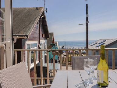 A balcony with a table holding a bottle of wine and two wine glasses overlooking houses and the sea at Grannys Teeth in Lyme Regis
