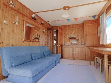 A room with wooden paneled walls a blue sofa a wooden cabinet model sailboats on walls and a wooden table with stools at Granny's Teeth Lyme Regis