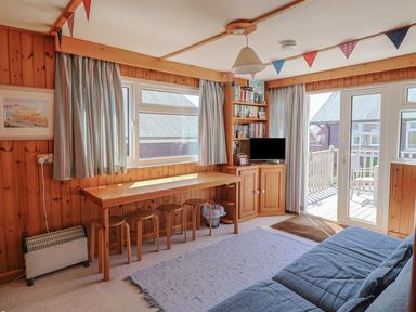 A living room with wooden panel walls a table with stools a television and a door leading to a deck at Grannys Teeth in Lyme Regis