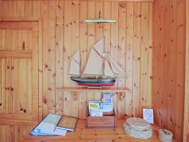 A wooden room with a model sailboat on a shelf above a wooden desk with books brochures and woven coasters at Grannys Teeth Lyme Regis