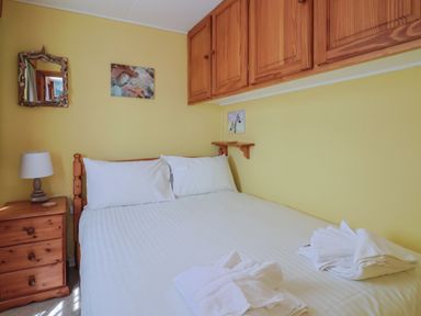 A bedroom with a double bed white linens wooden bedside table lamp wall cabinets and framed pictures at Grannys Teeth Lyme Regis