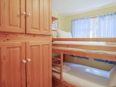 A bedroom with wooden bunk beds white bedding blue curtains and a wooden wardrobe at Granny's Teeth in Lyme Regis