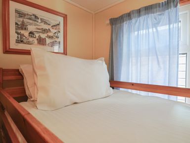 A wooden bunk bed with white pillows and a framed picture on the wall next to a window with light blue curtains at Grannys Teeth in Lyme Regis