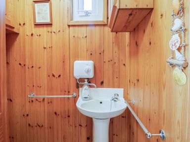 A small bathroom with wood-paneled walls a white pedestal sink a soap dispenser a towel bar and a small framed picture at Grannys Teeth in Lyme Regis