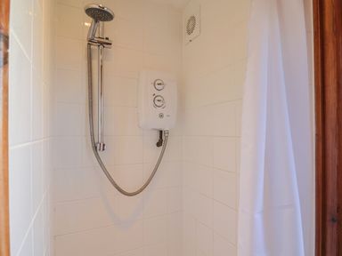 A shower area with a wall-mounted showerhead electric control unit and a white shower curtain at Grannys Teeth in Lyme Regis