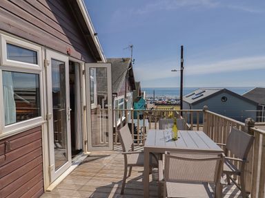 An outdoor wooden deck with a table and chairs and a bottle with glasses near the sea at Granny's Teeth Lyme Regis