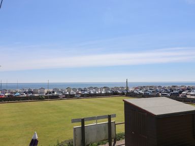 A grass field with a wooden shed near a parking lot and small beach huts by the sea at Granny's Teeth in Lyme Regis