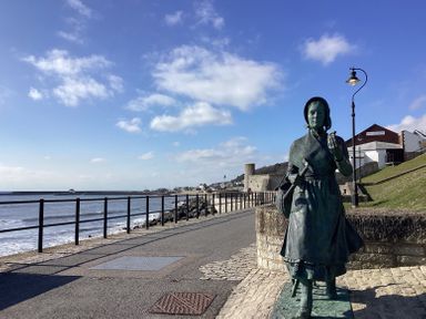 A coastal promenade with a statue of a woman holding a hammer and shell at Granny's Teeth in Lyme Regis