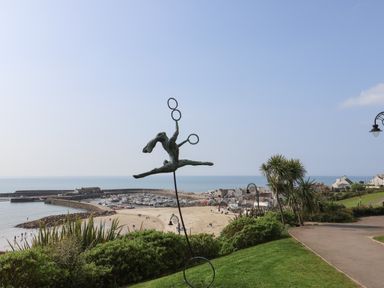 A coastal view with a sculpture of a person jumping with rings a beach marina and houses in the background at Grannys Teeth in Lyme Regis