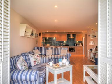 A living room with blue striped sofas and pillows and a kitchen with wooden cabinets and blue tile backsplash at 2 Buckfields in Lyme Regis