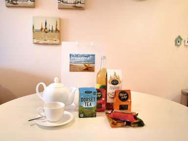 A table with a white teapot and cup a box of Dorset tea hand roasted coffee fudge and a welcome bag at 2 Buckfields in Lyme Regis