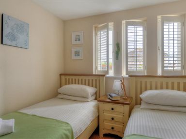 A bedroom with two single beds separated by a wooden nightstand with books and a lamp at 2 Buckfields Lyme Regis