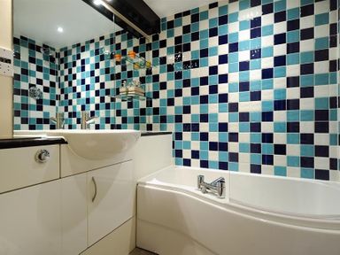 A bathroom with a bathtub sink and blue white checkered tiles on the wall at 2 Buckfields in Lyme Regis