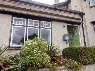 The exterior of a house with a green door and windows with plants and shrubs in front at The Apartment at Queen Anne's Lodge in Lyme Regis
