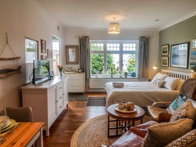 A bedroom with a bed a TV on a cabinet and a table with chairs at The Apartment at Queen Anne's Lodge in Lyme Regis