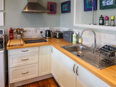 A kitchen countertop with a sink a drying rack a bread box a toaster and cooking utensils at The Apartment at Queen Anne's Lodge in Lyme Regis