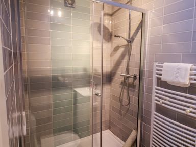 A bathroom with a glass shower enclosure a showerhead and a towel rack with a towel at The Apartment at Queen Anne's Lodge in Lyme Regis