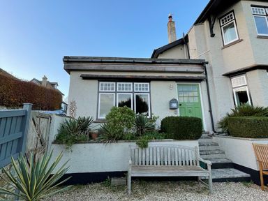 Front of a house with a green door, windows, plants, and a wooden bench in the garden at The Apartment at Queen Anne's Lodge in Lyme Regis