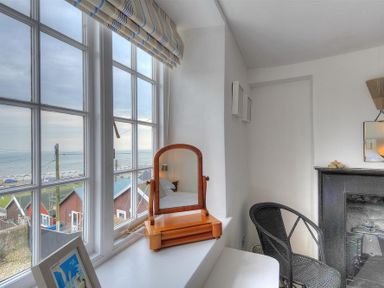 A room with a large window showing a seaside view a wooden mirror on the windowsill a black woven chair and a fireplace at 10 Cobb Terrace in Lyme Regis