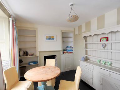 A dining room with a wooden oval table four yellow chairs built in shelves and a white cabinet at 10 Cobb Terrace Lyme Regis