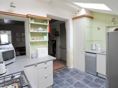 A kitchen with gray tile floor white cabinets dishwasher toaster kettle and open shelving with cups and teapot at 10 Cobb Terrace Lyme Regis