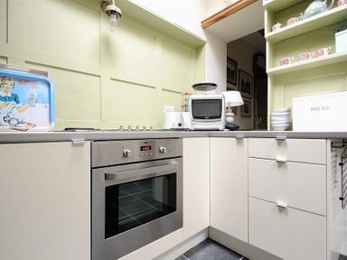 A kitchen corner with oven toaster toaster breadbin and shelves with mugs at 10 Cobb Terrace in Lyme Regis