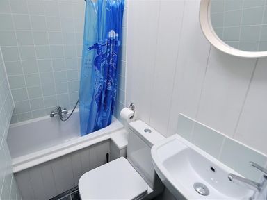 A bathroom with a bathtub, blue shower curtain, toilet, sink, and round mirror at 10 Cobb Terrace in Lyme Regis