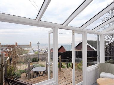 A conservatory with glass roof and white frames overlooking a garden with outdoor table and bench at 10 Cobb Terrace in Lyme Regis