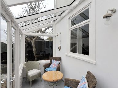 A sunroom with glass walls and ceiling containing two wicker chairs with cushions one armchair and a round wooden table at 10 Cobb Terrace in Lyme Regis