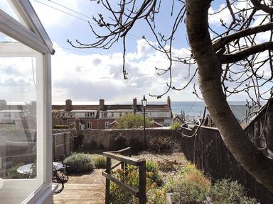 A garden with plants wooden fence and outdoor seating overlooking houses and the sea at 10 Cobb Terrace Lyme Regis