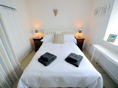 A bedroom with a white bed and striped pillow with nightstands and lamps on either side at 10 Cobb Terrace Lyme Regis