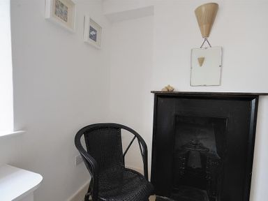 A black wicker chair next to a black fireplace with a mirror and light fixture above at 10 Cobb Terrace Lyme Regis