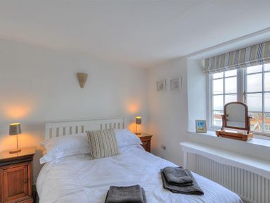 A bedroom with a white bed and striped pillow near a window with a mirror at 10 Cobb Terrace in Lyme Regis